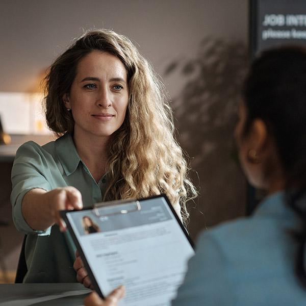 Woman handing her resume across a desk to a recruiter